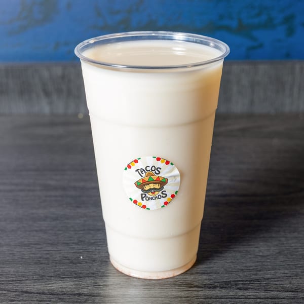 A Tacos Ponchos horchata drink in a clear plastic cup with the restaurant's logo sticker.