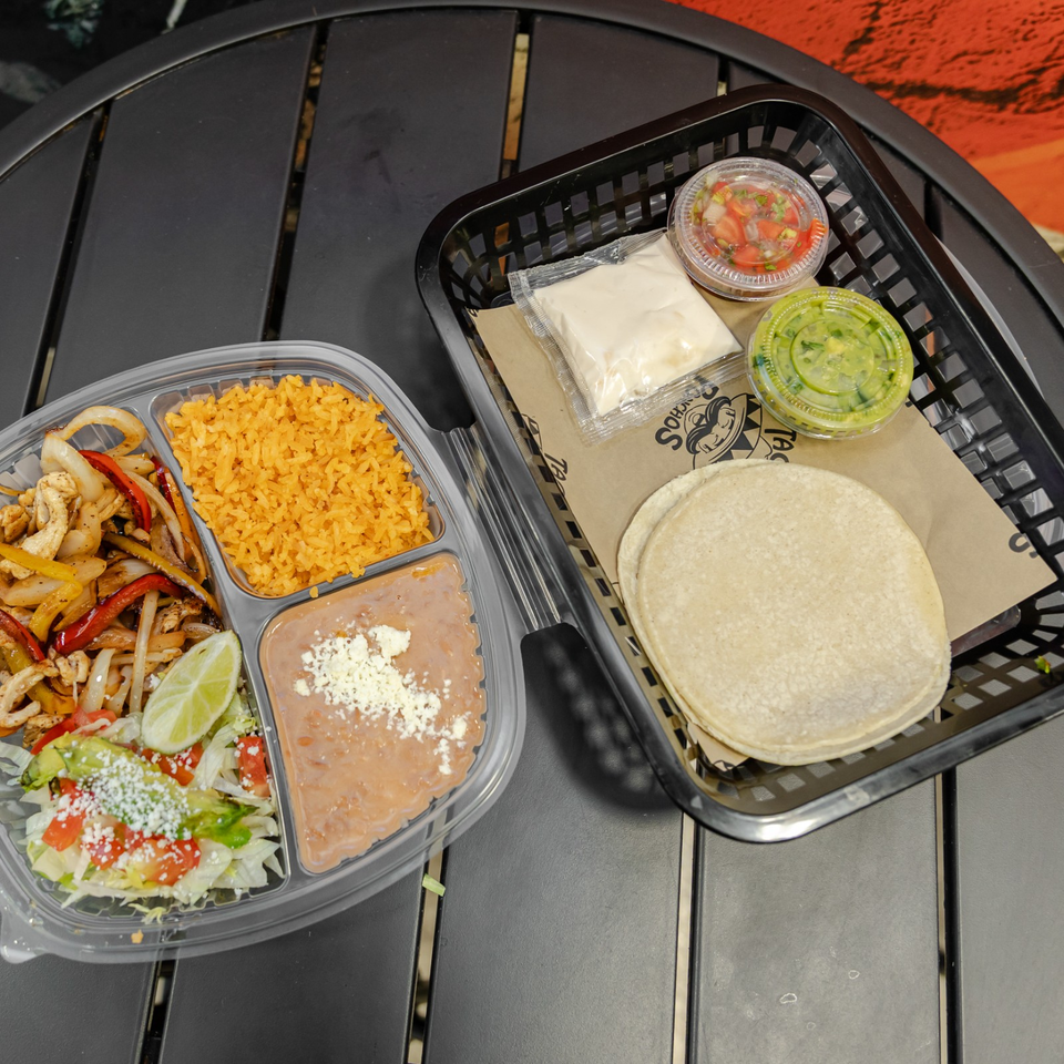 Mexican meal with chicken fajitas, yellow rice, refried beans, salad, lime, corn tortillas, cheese, salsa, and green sauce.