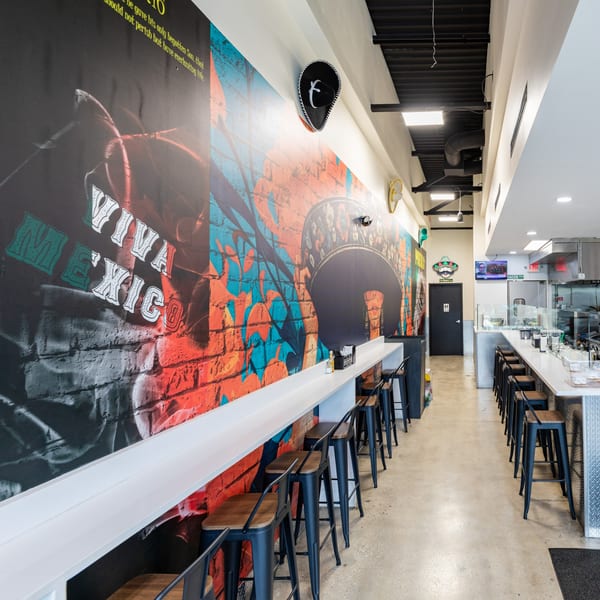 Interior of Tacos Ponchos with a long counter, bar stools, and a vibrant "Viva Mexico" mural.