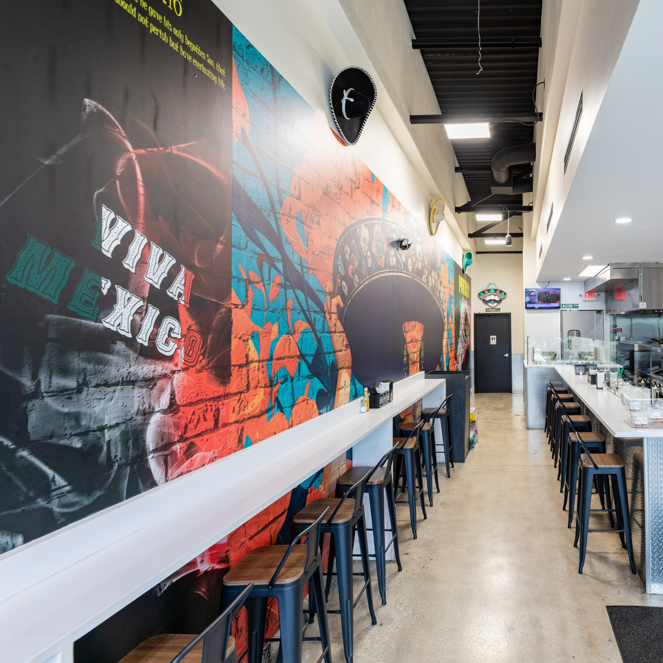 Interior of Tacos Ponchos with a long counter, bar stools, and a vibrant "Viva Mexico" mural.