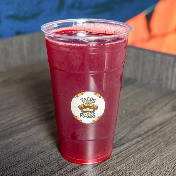 A plastic cup of red horchata with the Tacos Ponchos logo on a wooden table.
