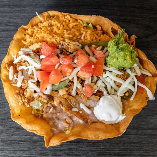 A Tacos Ponchos taco salad with chicken, rice, beans, cheese, tomatoes, guacamole, and sour cream.