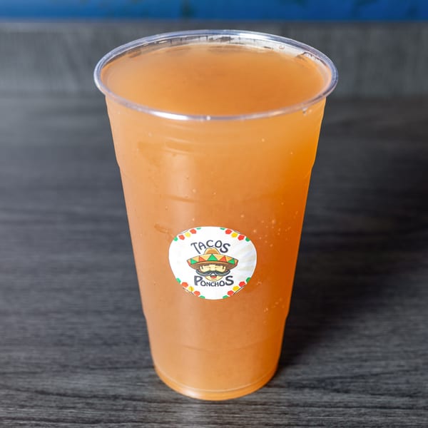 A plastic cup of orange-colored drink with a Tacos Ponchos logo sticker on a dark wooden surface.