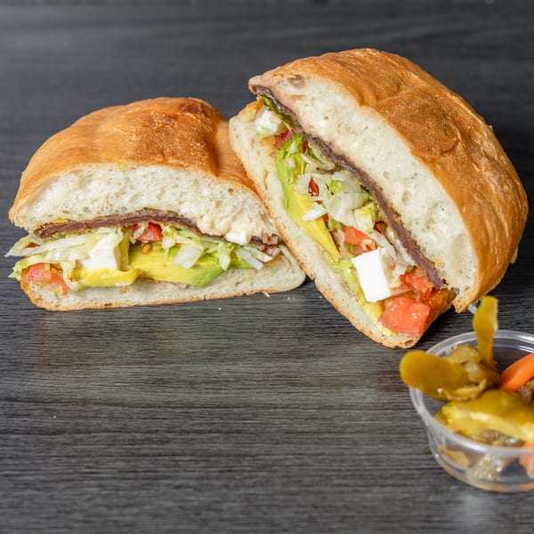 A Tacos Ponchos Mexican torta, sliced in half, with avocado, lettuce, tomato, and cheese.