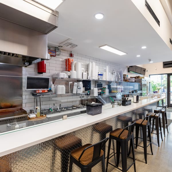 Interior of Tacos Ponchos showing a long counter with bar stools and kitchen prep area.