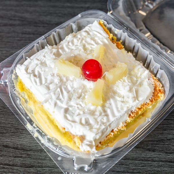 A square slice of Tres Leches cake with whipped cream, pineapple chunks, and a cherry on top.