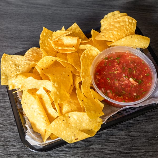 A black tray filled with golden tortilla chips and a clear plastic container of red salsa.