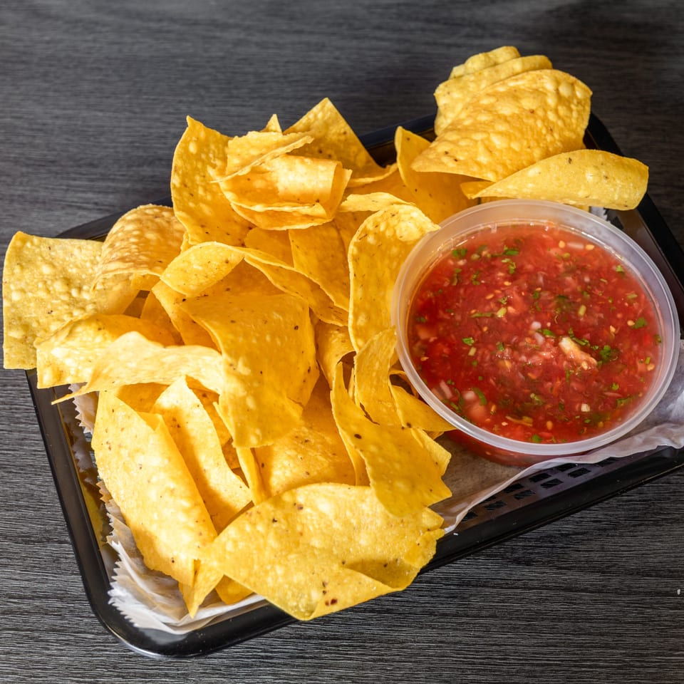 A black tray filled with golden tortilla chips and a clear plastic container of red salsa.