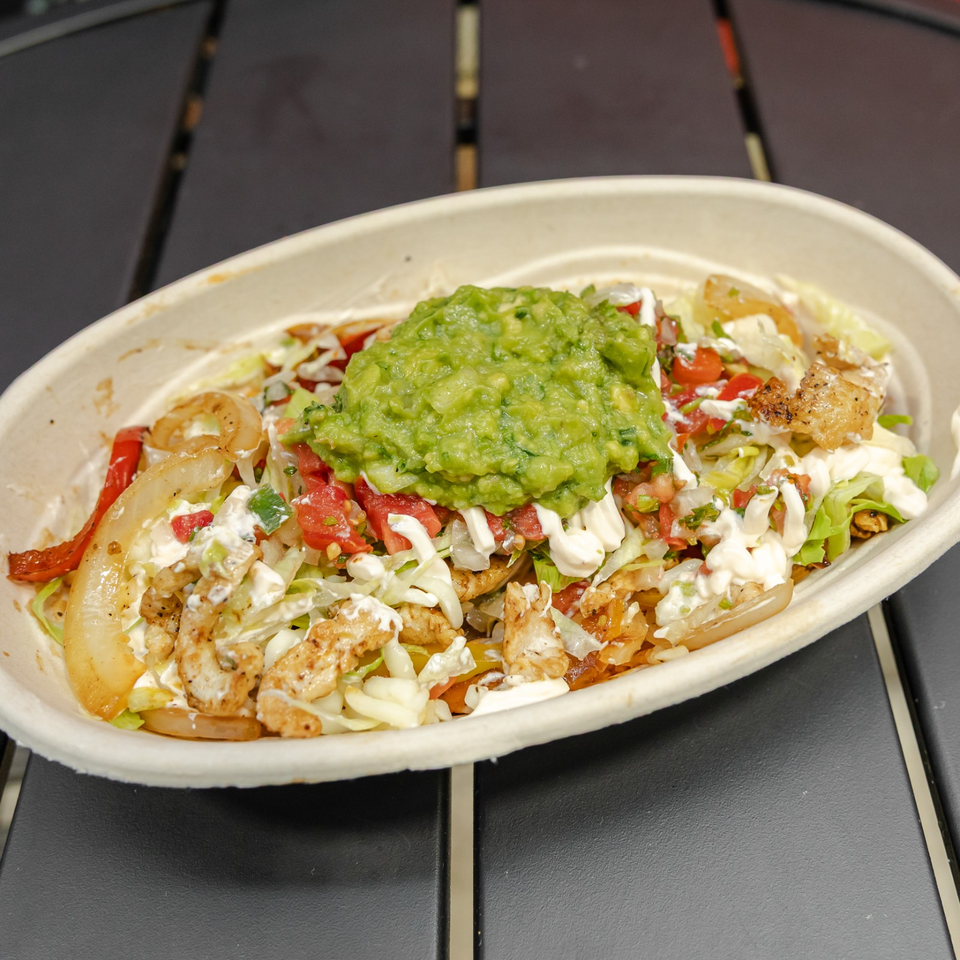 Loaded Mexican-style platter with grilled chicken, onions, tomatoes, lettuce, creamy sauce, and guacamole in a bowl.