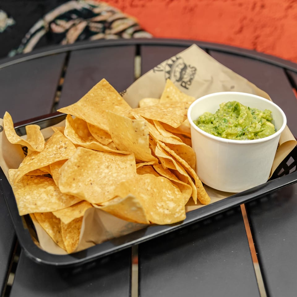Basket of crispy tortilla chips served with a cup of chunky guacamole on a restaurant table.
