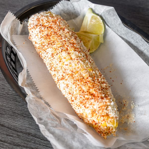 Elote, Mexican street corn, topped with cotija cheese and chili powder, served with lime wedges.
